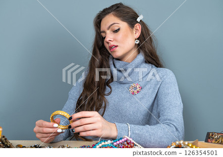 young brunette sitting at the table with lots of jewelry, choosing and trying different jewelry young brunette sitting at the table with lots of jewelry, choosing and trying different jewelry 126354501