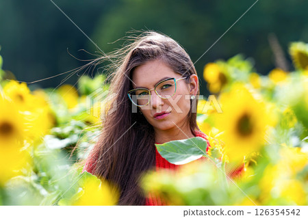 pretty sensual young brunette in a field of sunflowers in a red sweater, happy woman outdoors 126354542