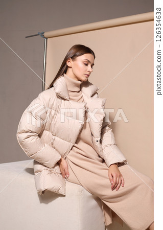 beautiful fashion female model in beige down jacket and long wool turtleneck dress in studio. Autumn winter total fashion beige look beautiful fashion female model in beige down jacket and long wool turtleneck dress in studio. Autumn winter total fashion beige look 126354638