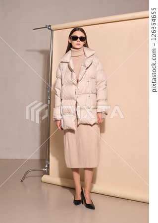 beautiful fashion female model in beige down jacket and long wool turtleneck dress in studio. beautiful fashion female model in beige down jacket and long wool turtleneck dress in studio. 126354655