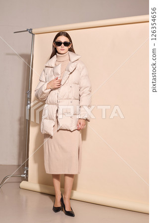 beautiful fashion female model in beige down jacket and long wool turtleneck dress in studio. beautiful fashion female model in beige down jacket and long wool turtleneck dress in studio. 126354656