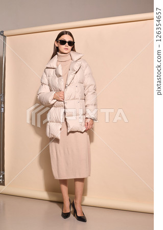 beautiful fashion female model in beige down jacket and long wool turtleneck dress in studio. beautiful fashion female model in beige down jacket and long wool turtleneck dress in studio. 126354657