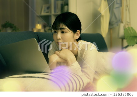 Young woman looking at laptop on sofa at night 126355003