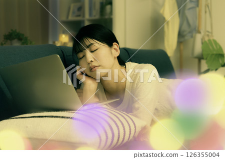 A young woman falls asleep on the sofa at night while looking at a laptop 126355004