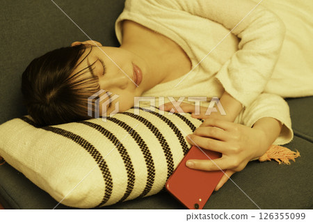 A young woman falls asleep on the sofa at night while looking at her smartphone 126355099