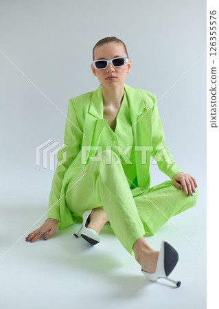 High fashion portrait of young confident female model in green lime color three-piece suit. Monochrome green outfit 126355576