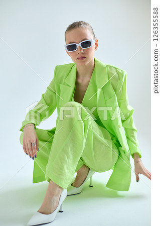 High fashion portrait of young confident female model in green lime color three-piece suit. Monochrome green outfit 126355588