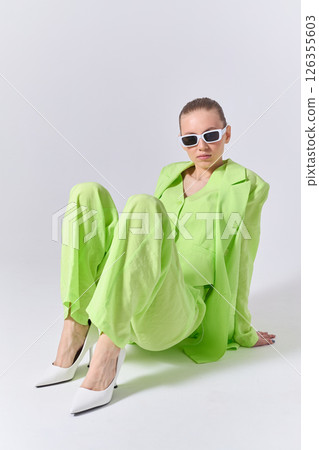 High fashion portrait of young confident female model in green lime color three-piece suit. Monochrome green outfit 126355603