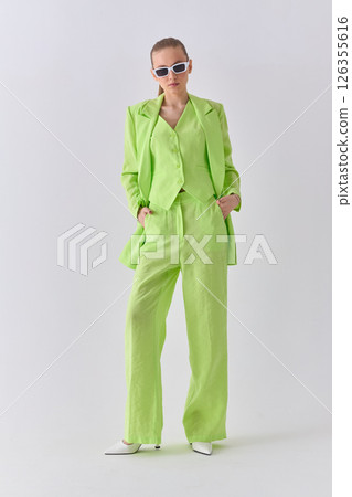 High fashion portrait of young confident female model in green lime color three-piece suit. Monochrome green outfit 126355616
