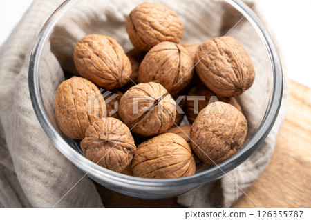 Full glass bowl with whole walnuts on fabric tablecloth. Close-up. Top view Full glass bowl with whole walnuts on fabric tablecloth. Close-up. Top view 126355787