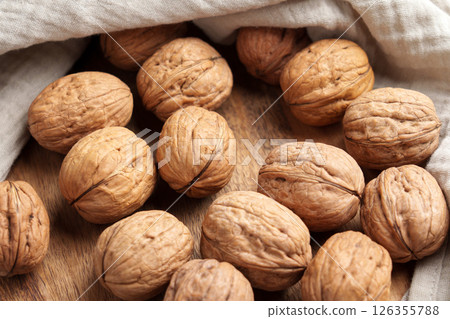 Pile of whole unshelled walnuts on wooden table with crumpled cloth napkin. Top view Pile of whole unshelled walnuts on wooden table with crumpled cloth napkin. Top view 126355788