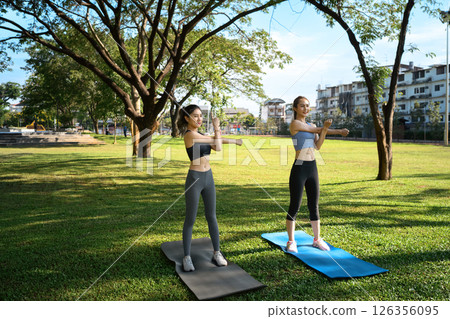 Two young women stretching outdoors on yoga mats in a city park 126356095