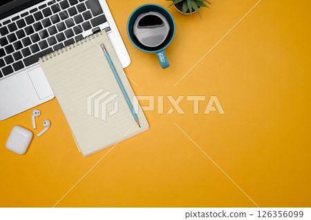 Creative workspace with laptop, notebook, coffee mug and wireless earbuds on yellow background 126356099
