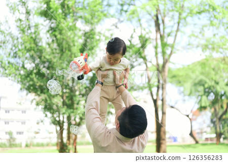 joyful dad lifts his toddler high in the air as the child holds a bubble gun joyful dad lifts his toddler high in the air as the child holds a bubble gun 126356283