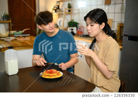 Romantic couple enjoying pancake breakfast together in a cozy kitchen Romantic couple enjoying pancake breakfast together in a cozy kitchen 126356330