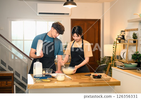 Cheerful young couple preparing pancake batter together in kitchen Cheerful young couple preparing pancake batter together in kitchen 126356331