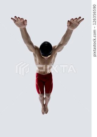 Male swimmer with arms extended wide and head lowered, demonstrating balance, muscle control and preparation for dive against white background. 126356590