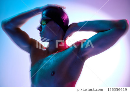 Side view portrait of intense male swimmer gazing forward with neon reflections on face and shoulders against gradient background. 126356619