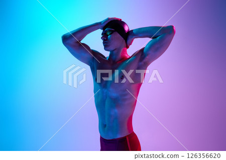 Athletic man, swimmer adjusts goggles with calm expression and intense gaze in vibrant neon light against gradient background. 126356620