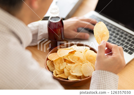 A middle-aged man working while eating potato chips A middle-aged man working while eating potato chips 126357030