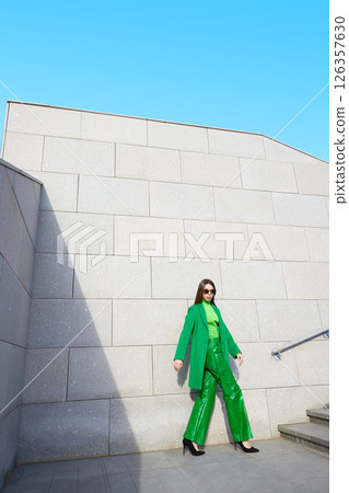 High fashion photo of a young brunette woman in green coat, poloneck and leather pants. 126357630