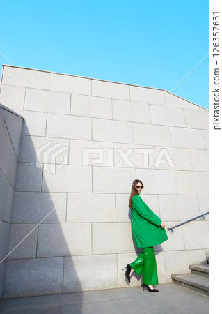 High fashion photo of a young brunette woman in green coat, poloneck and leather pants. 126357631