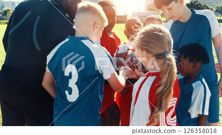 Hands together, football and coach in huddle with children on field for motivation, game plan and strategy. Competition, training and practice with kids outdoor for sports, soccer player and support Hands together, football and coach in huddle with children on field for motivation, game plan and strategy. Competition, training and practice with kids outdoor for sports, soccer player and support 126358018