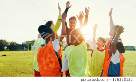 Hands up, soccer and coach in huddle with happy kids on field for motivation, game plan or strategy. Excited, training and practice with children in celebration for sports, football player or support 126358123