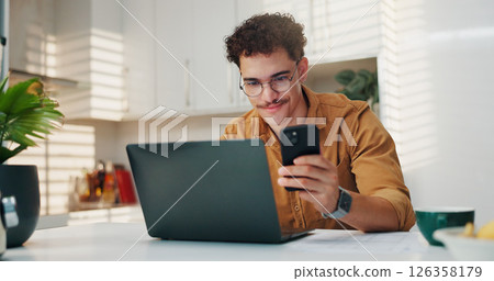 Home, smartphone and man in kitchen, laptop and website info with creativity, online research and connection. Social media, freelancer or person with pc, cellphone and feedback for proposal or review 126358179