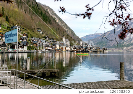 Scenic view of Hallstatt village in Austria with traditional houses nestled between mountains and lake. Church spires wooden dock in foreground calm water reflecting buildings. Scenic view of Hallstatt village in Austria with traditional houses nestled between mountains and lake. Church spires wooden dock in foreground calm water reflecting buildings. 126358260