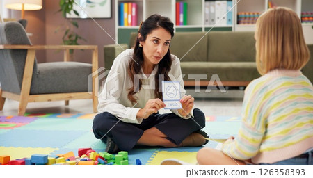 Woman, girl and card with psychology for emotion, choice or sad emoji for mental health assessment on floor. Paper, therapist and child with sign for feelings, icon and evaluation with test at clinic 126358393