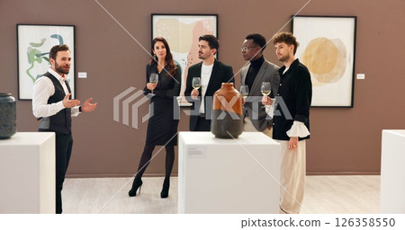 Man, explain and people with champagne at gallery for event, audience chat and talking for auction. Curator, customer and alcohol for discussion, artwork collection and art presentation of exhibition Man, explain and people with champagne at gallery for event, audience chat and talking for auction. Curator, customer and alcohol for discussion, artwork collection and art presentation of exhibition 126358550