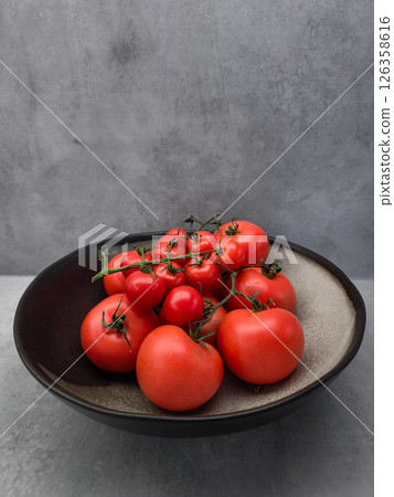 Ripe red tomatoes clustered on vine, nestled in black ceramic bowl, showcasing garden fresh produce against minimalist background wallpaper copy space Ripe red tomatoes clustered on vine, nestled in black ceramic bowl, showcasing garden fresh produce against minimalist background wallpaper copy space 126358616