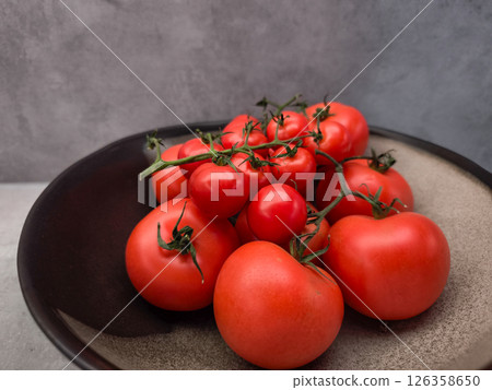 Ripe red tomatoes and cherry tomatoes on the vine, presented on a dark plate, creating a vibrant display of freshness 126358650