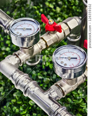 Pressure gauges and valves displayed on a metal piping system surrounded by lush greenery 126359102