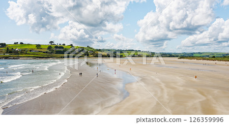 The idyllic beach scene reveals people relaxing and enjoying the weather. The serene atmosphere is enhanced by the rolling hills in the distance. 126359996