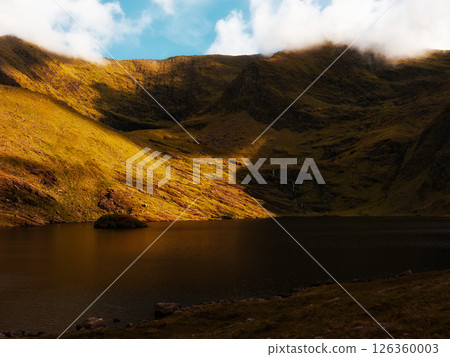 Lough Callee presents a striking landscape with still waters reflecting hills. The surrounding terrain exhibits vibrant colors and shadows, creating a picturesque view in Irish nature. Lough Callee presents a striking landscape with still waters reflecting hills. The surrounding terrain exhibits vibrant colors and shadows, creating a picturesque view in Irish nature. 126360003