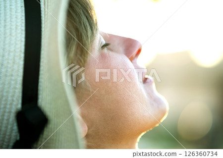 Young woman relaxing outdoors on sunny summer day. Happy lady in straw hat daydreaming thinking. Calm beautiful smiling girl enjoying fresh air relax with closed eyes. Young woman relaxing outdoors on sunny summer day. Happy lady in straw hat daydreaming thinking. Calm beautiful smiling girl enjoying fresh air relax with closed eyes. 126360734