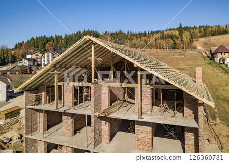 Wooden frame of new roof on a brick big house under construction. 126360781