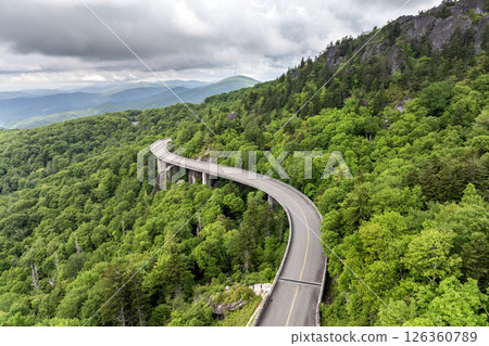 Winding mountain road in summer woods. Linn Cove Viaduct in Appalachian mountains in North Carolina with fresh green forest trees in summertime season. Beauty of USA nature Winding mountain road in summer woods. Linn Cove Viaduct in Appalachian mountains in North Carolina with fresh green forest trees in summertime season. Beauty of USA nature 126360789