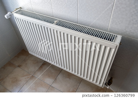 White metal heating radiator mounted on a wall in room interior. White metal heating radiator mounted on a wall in room interior. 126360799