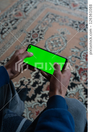 Guy is sitting with a smartphone in his hands with the green screen turned on 126361088