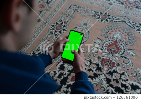 Guy is sitting with a smartphone in his hands with the green screen 126361090