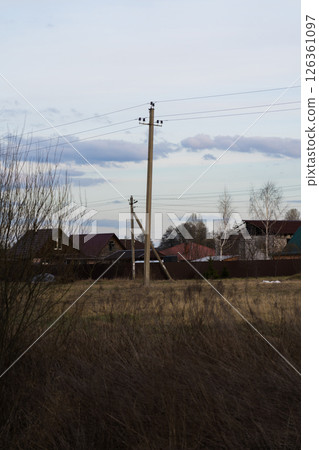 A power pole stands in a field, and houses are behind it 126361097