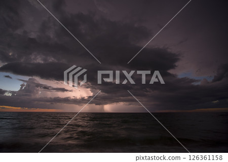 Thunderstorm dark clouds with lightning and thunder over evening sea water waves crushing on sandy beach. Seascape weather at sunset Thunderstorm dark clouds with lightning and thunder over evening sea water waves crushing on sandy beach. Seascape weather at sunset 126361158