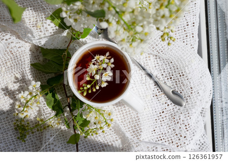 Delicate white flowers float on top of a steaming cup of tea surrounded by greenery on a sunny day 126361957