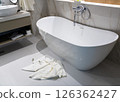 A freestanding modern bathtub with white towels left on the bathroom floor after use 126362427