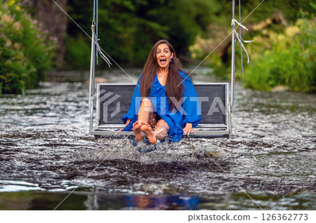 a joyful young woman swings on a rope swing across a fast-flowing river 126362773