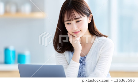 A woman looking at a laptop in the kitchen and planning dinner 126363596