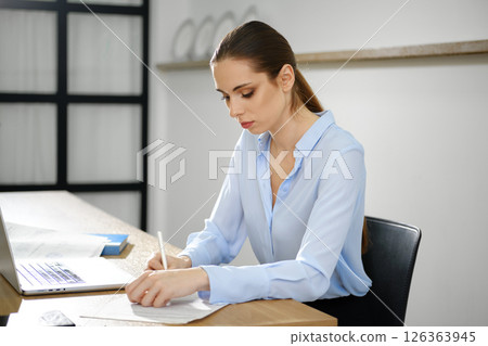 Focused business woman working diligently at a modern desk in a bright office space during the day 126363945